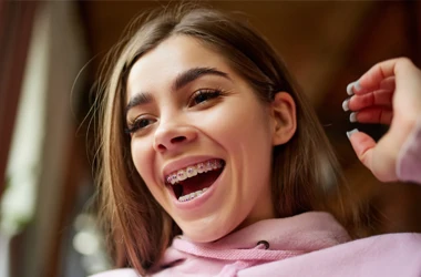 Orthodontist Ellicott City MD Girl In Pink Braces A girl smiling big in a pink sweatshirt. She has pink braces.