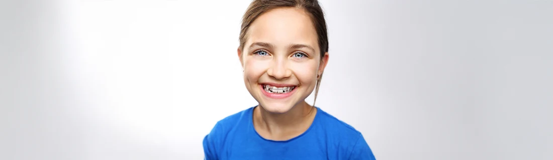 Orthodontist Ellicott City MD Smiling Young Girl 1 A young girl in a blue shirt smiling while wearing a metal retainer.