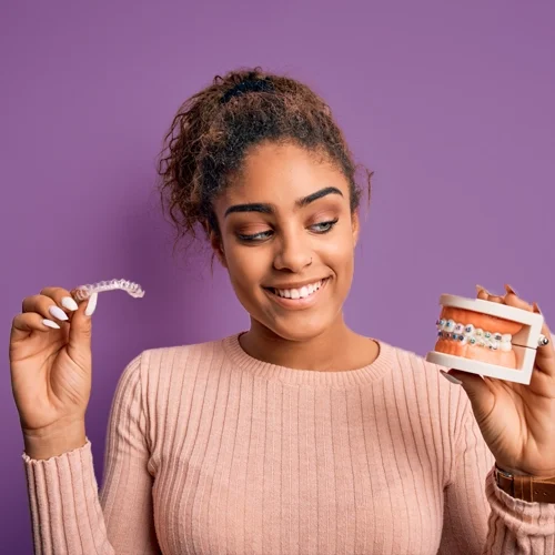 Orthodontist Ellicott City MD Young Adult A girl holding clear aligners in one have and a model of a mouth with braces in the other hand.