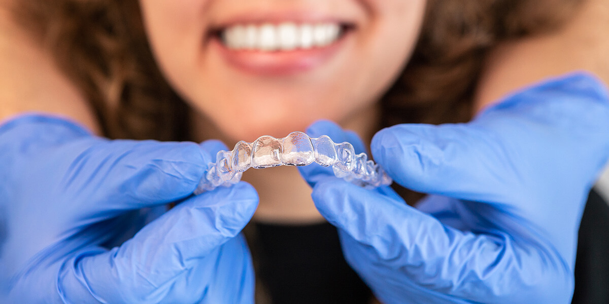 dentist holding clear aligner tray in front of patient's straight teeth